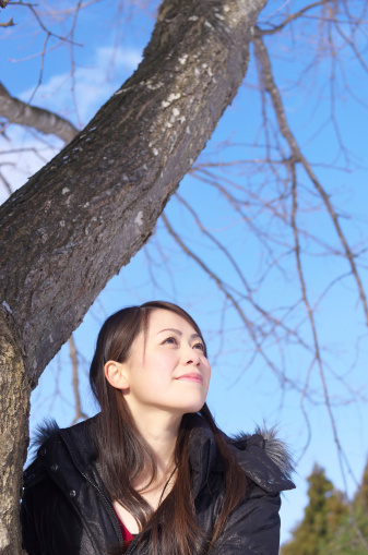 Young Asian woman beside tree trunk.