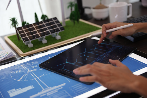 the professional working on a tablet with a black screen mock-up display. Creating a Concept of Wind Turbine and solar panel energy in an Office.