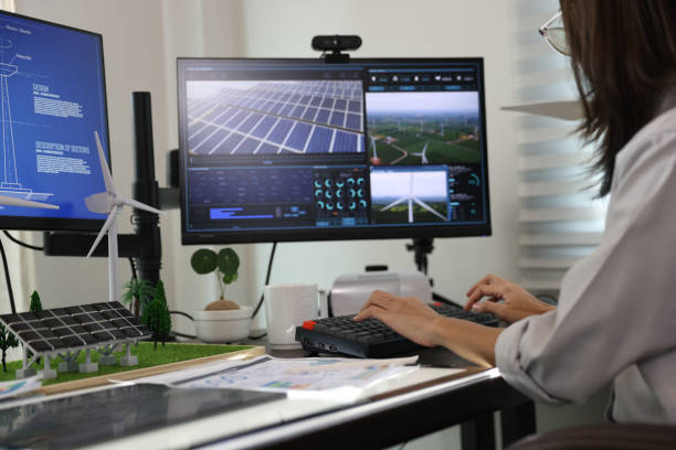 Female engineer with eyeglasses pensive thinking about her project on a personal computer, measuring layout on the digital program on a laptop, sitting in an office or co-working space, working hard in wind turbine background.