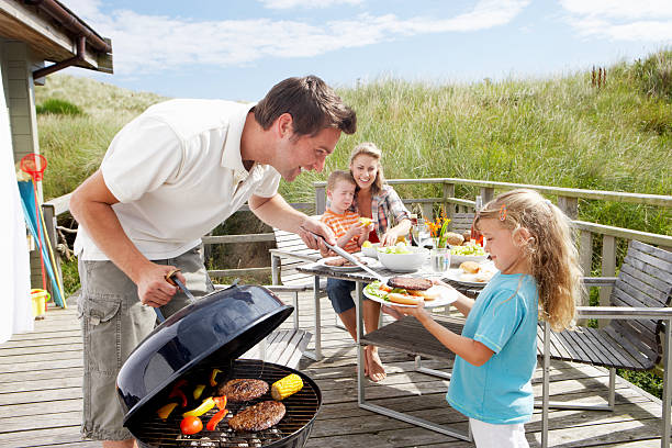 Family on vacation having barbecue Family on vacation having barbecue sitting on decking family bbq beach stock pictures, royalty-free photos & images