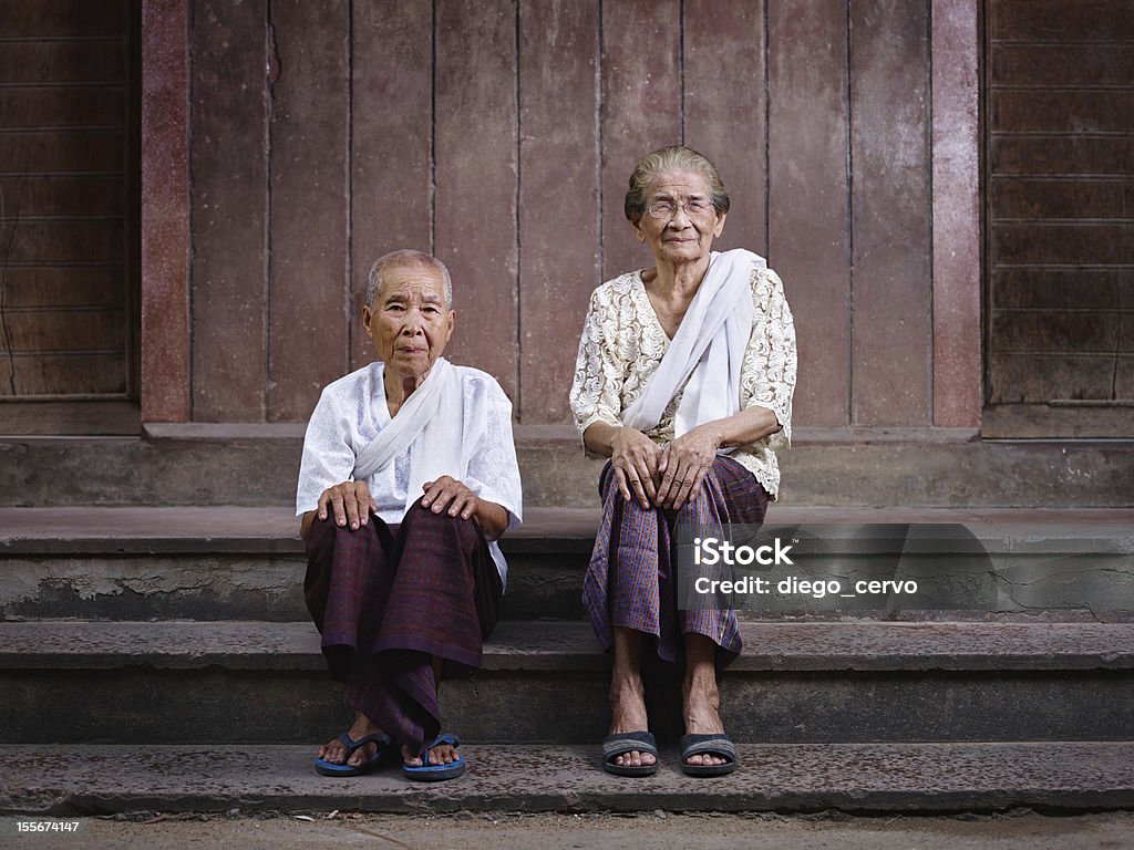 Portrait of two senior asian women looking at camera Portrait of two old asian women sitting on steps out of their house and looking at camera Family Stock Photo