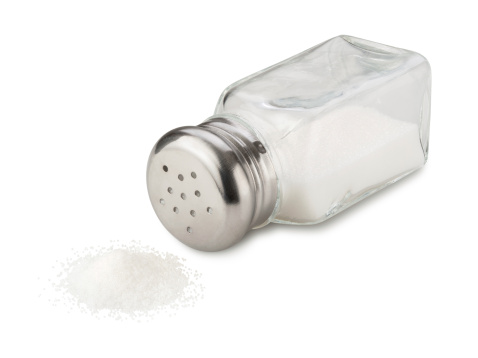 Salt shaker spilling salt. Salt is a spice used for seasoning for preserving food. The image is shown at an angle, and is in full focus from front to back. The image is isolated on a white background, and includes a clipping path.