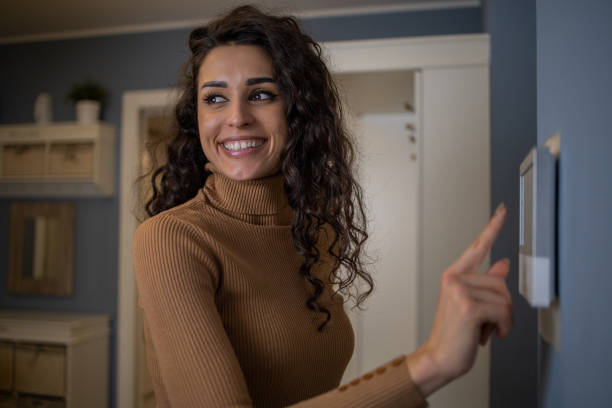 istock Young woman adjusts the temperature at home with a device on the wall 1556874516