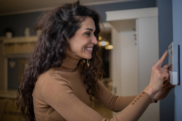 istock Young woman adjusts the temperature at home with a device on the wall 1556874518
