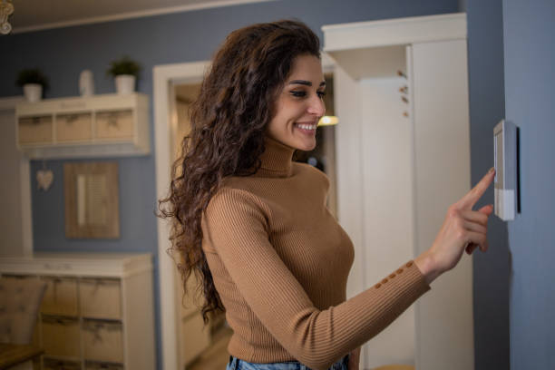 istock Young woman adjusts the temperature at home with a device on the wall 1556874523