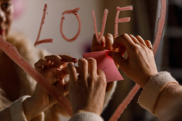 Woman applying a sticky note with the words ''miss you'' on the mirror Close up shot of unrecognizable woman applying a sticky note with the words ''miss you'' inside a lipstick drawn heart with the word ''love'' written in the middle, on the mirror. mirror writing stock pictures, royalty-free photos & images