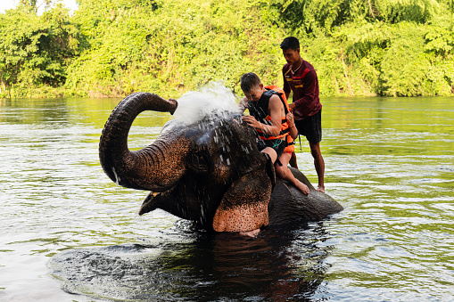 Elephant spraying water to people during riding. Children swim with an elephant in the river Kwai. Thailand. July 5, 2023.