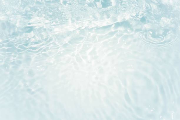 Blue water with ripples on the surface. Defocus blurred transparent blue colored clear calm water surface texture with splashes and bubbles. Water waves with shining pattern texture background.