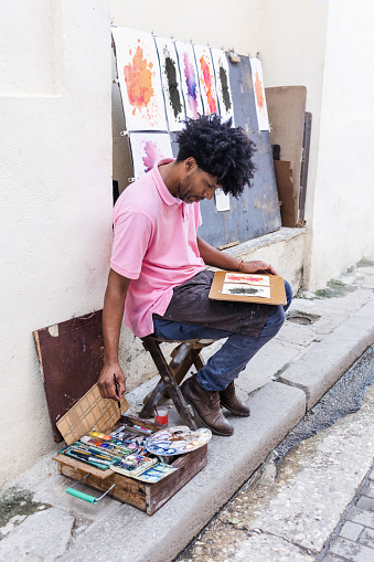 african american man artist or painter in the street painting on footpath in Latin America, Afro caribbean male drawing street art