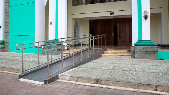 Ramp with stainless steel handrail at the main entrance of a mosque to enable a disabled wheelchair user to access it.