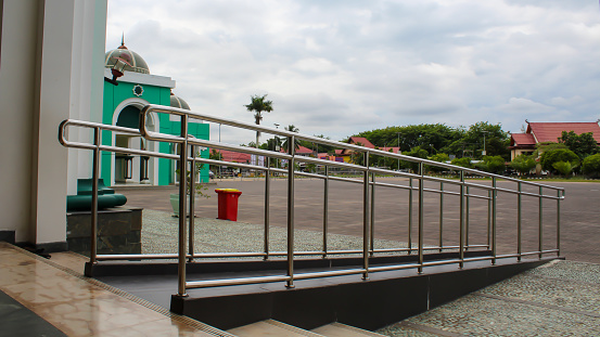 Ramp with stainless steel handrail at the main entrance of a mosque to enable a disabled wheelchair user to access it.