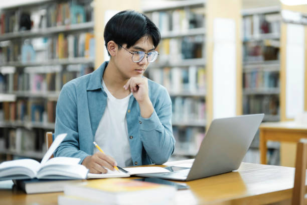 istock Young university student using laptop for online learning, searching and learning at library. 1557131750