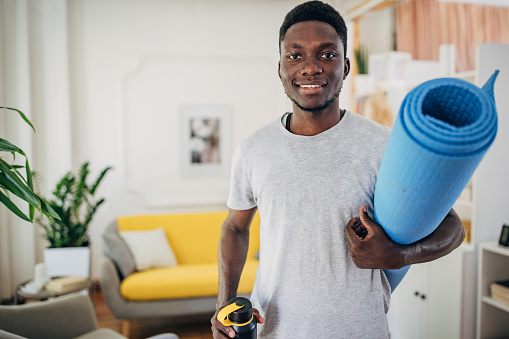 Man holding exercise mat and water bottle at home.