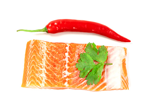 Piece of fresh salmon fillet sliced with coriander leaves and red pepper isolated on white background