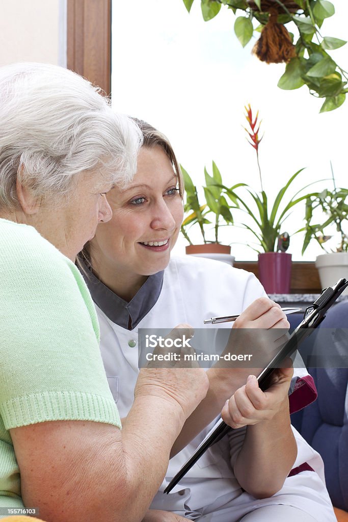 Sênior com a enfermeira sentar-se juntos e escreva os dados - Foto de stock de 70 anos royalty-free