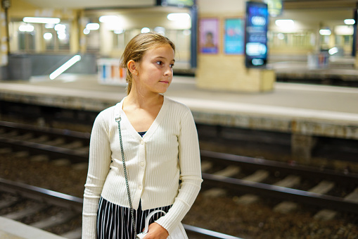 Little stylish cute girl waiting for train at evening station.
