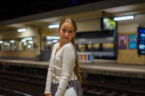 Little stylish cute girl waiting for train at evening station.