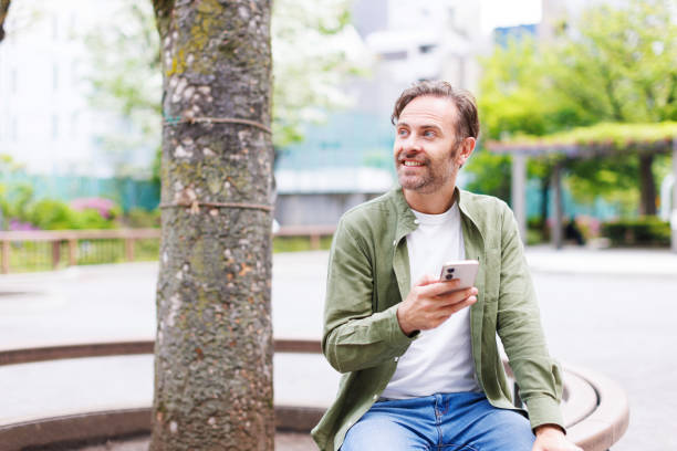 istock Caucasian man with mobile phone sitting outdoors 1557213949