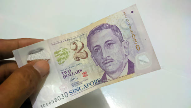istock A man's hand is holding a Singapore dollar banknote on a white background. 1557221656