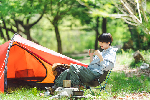 Young Asian woman is doing solo camping and drinking.