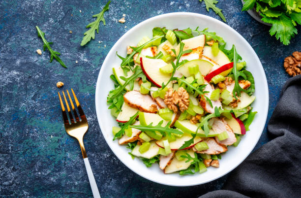 istock Waldorf salad with fresh apple, celery, lettuce, grilled chicken fillet, arugula and walnuts on plate, blue table background, top view 1557237508