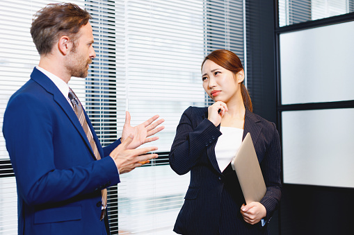 Two smiling business people walking through office hall and talking