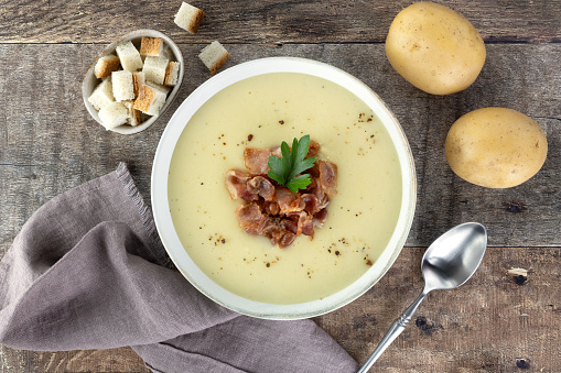 Creamy potato soup with bacon, croutons, ingredients on a wooden background. Top view. French vichyssoise soup.