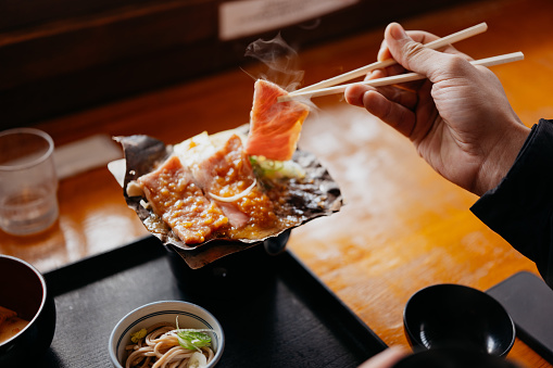 Close up shot of hand of a man grilling Hida beef on hoba miso in a Japanese restaurant