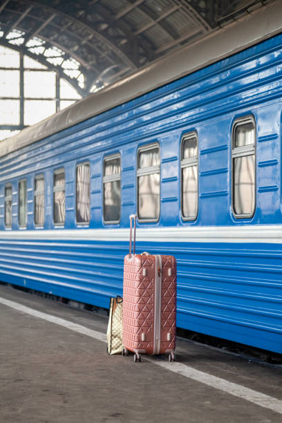 A modern suitcase on wheels with a long handle stands on an empty platform in front of a blue carriage