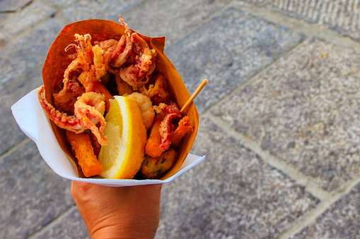 Typical Italian appetizer (Fritto misto di pesce) mix of fried seafood i female hand. Healthy snack in Genoa, Cinque Terre and Portofino