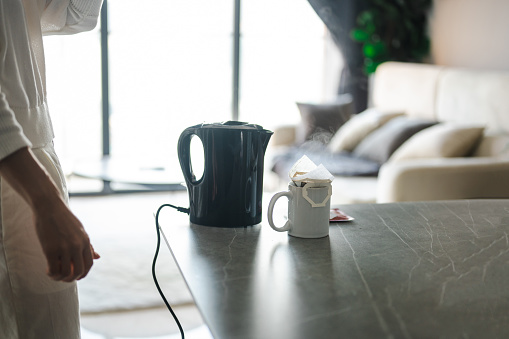 Making coffee with drip coffee bag in a beige cup on white marble table