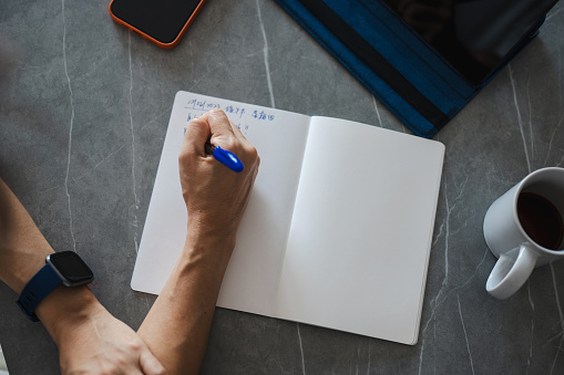 A woman is writing a diary note with a digital tablet while enjoying coffee at home.