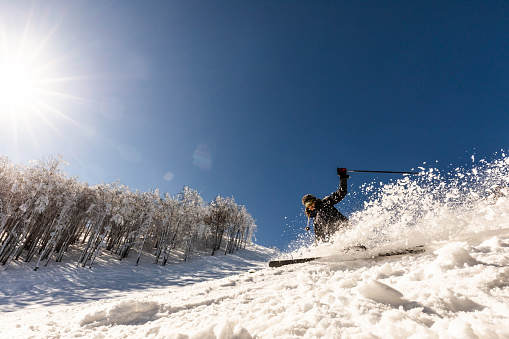 Low angle view of carefree woman having fun while skiing and splashing snow on a mountain. Copy space.