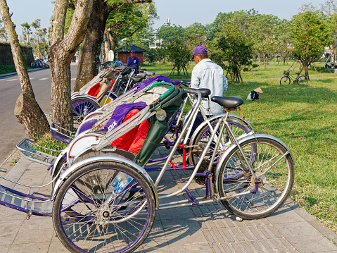 Hue, Vietnam - March 22, 2023: Trishaws are parked on the footpath in front of the Imperial Citadel while the riders wait for their passengers who make a tour inside the citadel.
