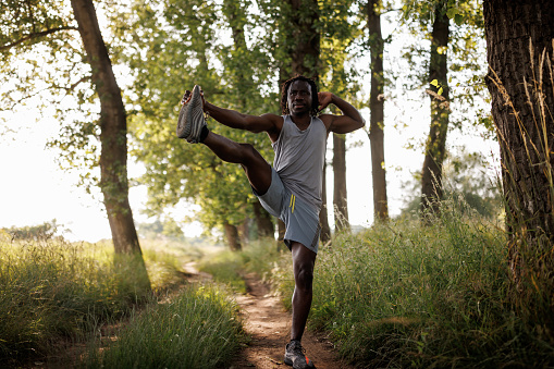 Full length shot of young African man warming up before jogging in nature