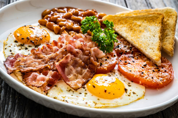 istock English breakfast - sunny side up eggs,bacon, beans, toasts and fried tomatoes on wooden table 1557424764