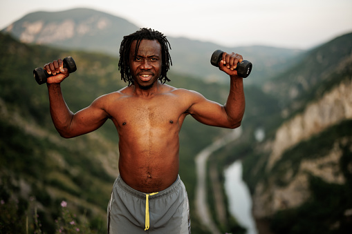 Young African man working out with  dumbbells in nature