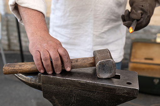 An unrecognizable blacksmith forges hot metal with a hammer on an anvile.