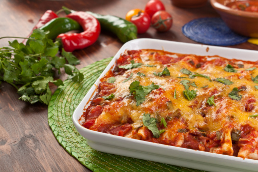 dish with traditional mexican food enchiladas baked with tomato salsa and cheddar cheese and ingredients on a table