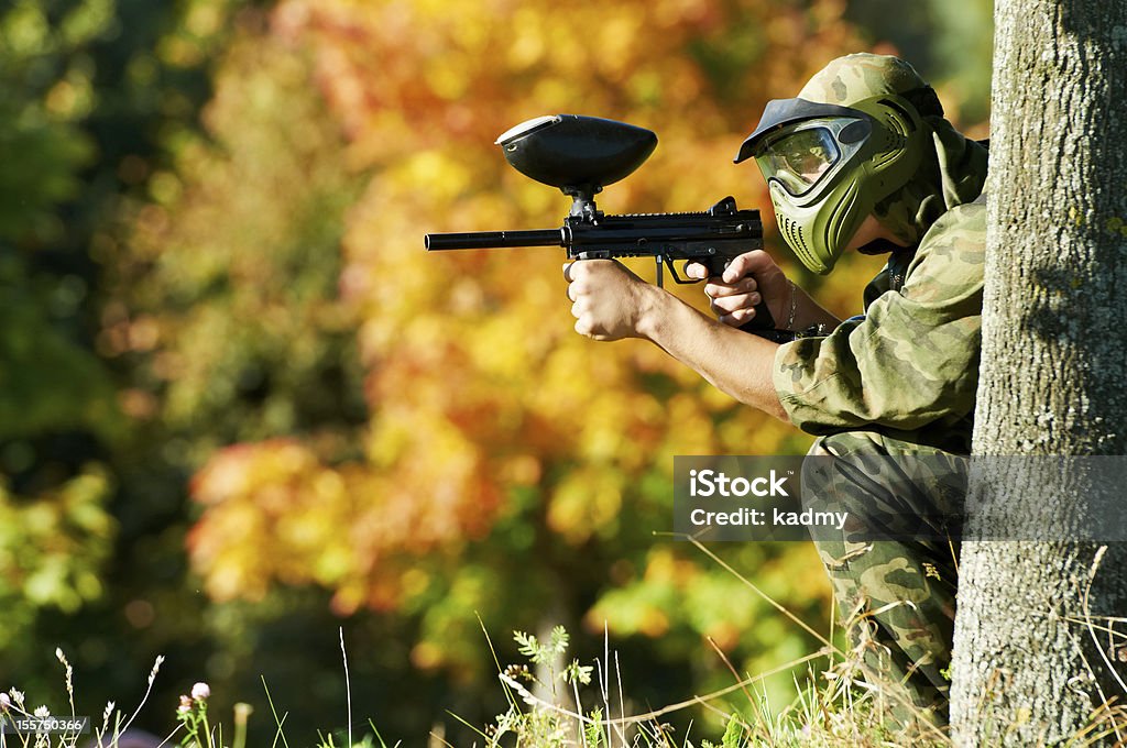 paintball player paintball sport player in protective uniform and mask aiming and shooting with gun outdoors Paintballing Stock Photo