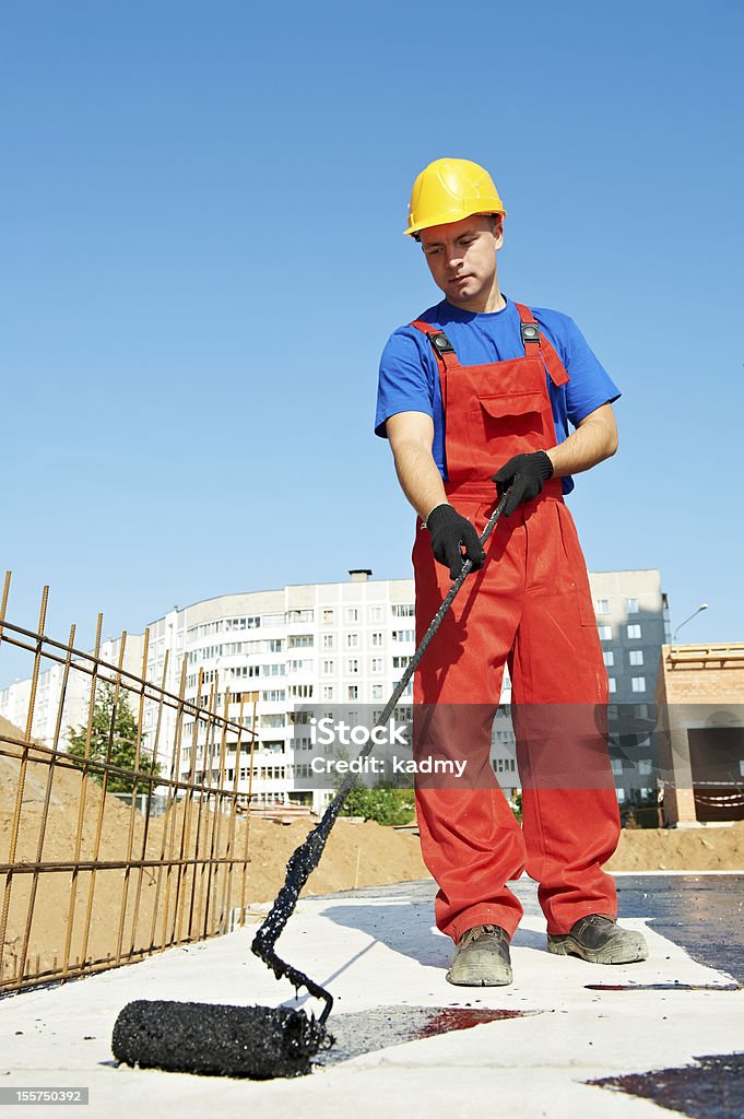 builder worker at roof insulation work builder worker in uniformcovering roof with insulation tar material at construction site Painting - Activity Stock Photo