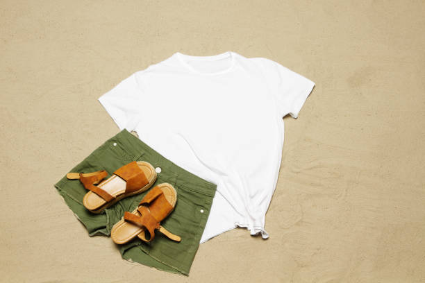 istock Sand beach texture background. Mockup white summer t-shirt copy space. Blank template woman shirt Top view. Summertime accessories jeans, sandals. Flat-lay closeup tshirt seashore. Beachtime 1557513395