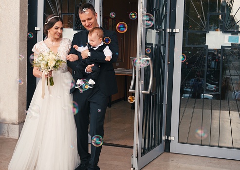 Just married couple with just baptized child going out of the church with soap bubbles in front of them