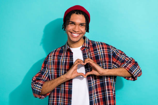 ritratto fotografico delle mani del giovane ragazzo bello che mostra le dita a forma di cuore vestite eleganti vestiti a scacchi isolati su priorità bassa di colore ciano - fun knit hat adult dating foto e immagini stock