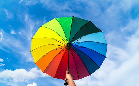 Hand holding colorful rainbow umbrella and blue sky background. LGBT, Pride Month, diversity, Sunprotect Concept.