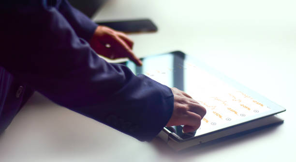 istock A young man in a robe operates a digital schematic screen of a mobile tablet with his hands. And use your hand to scroll the screen and see the stock chart that is currently displayed. 1557557785