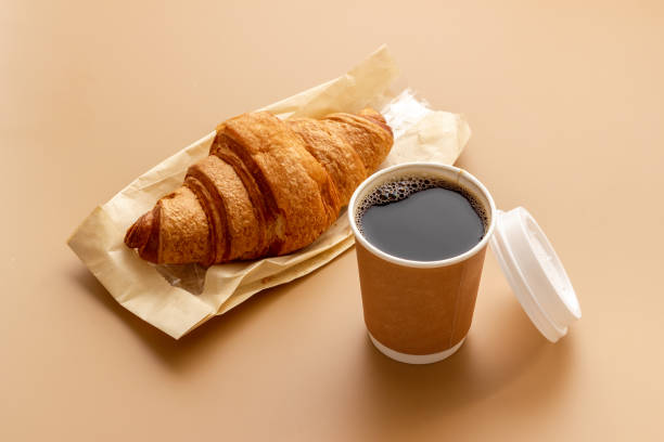 istock Takeaway coffee in paper cup with croissant. Coffee break background 1557604676