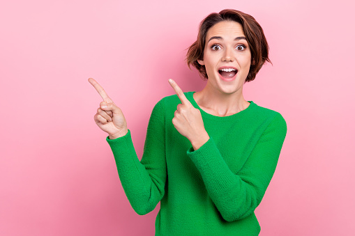 Photo of young surprised girl wear green jumper shocked impressed reaction indicate fingers empty space isolated on pink color background.