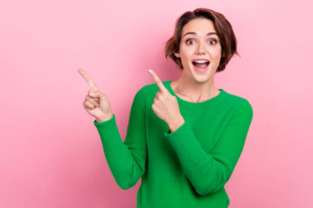 Photo of young surprised girl wear green jumper shocked impressed reaction indicate fingers empty space isolated on pink color background stock photo