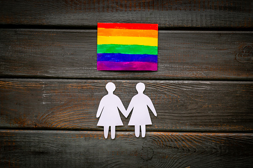 Gay pride rainbow LGBT flag with women couple paper shapes. LGBT social rights concept